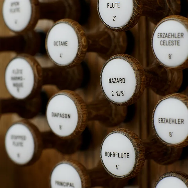 Nærbilde av et kirkeorgelpanel i tre med mange knapper for å spille musikk.